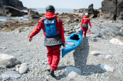 Carrying a sea kayak over rocks wearing the Palm Bora Suit